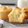 Freshly baked golden muffins cooling on a wire rack with a fluffy interior.