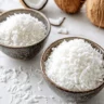 A bowl of sweetened coconut and a bowl of unsweetened coconut on a white marble counter.